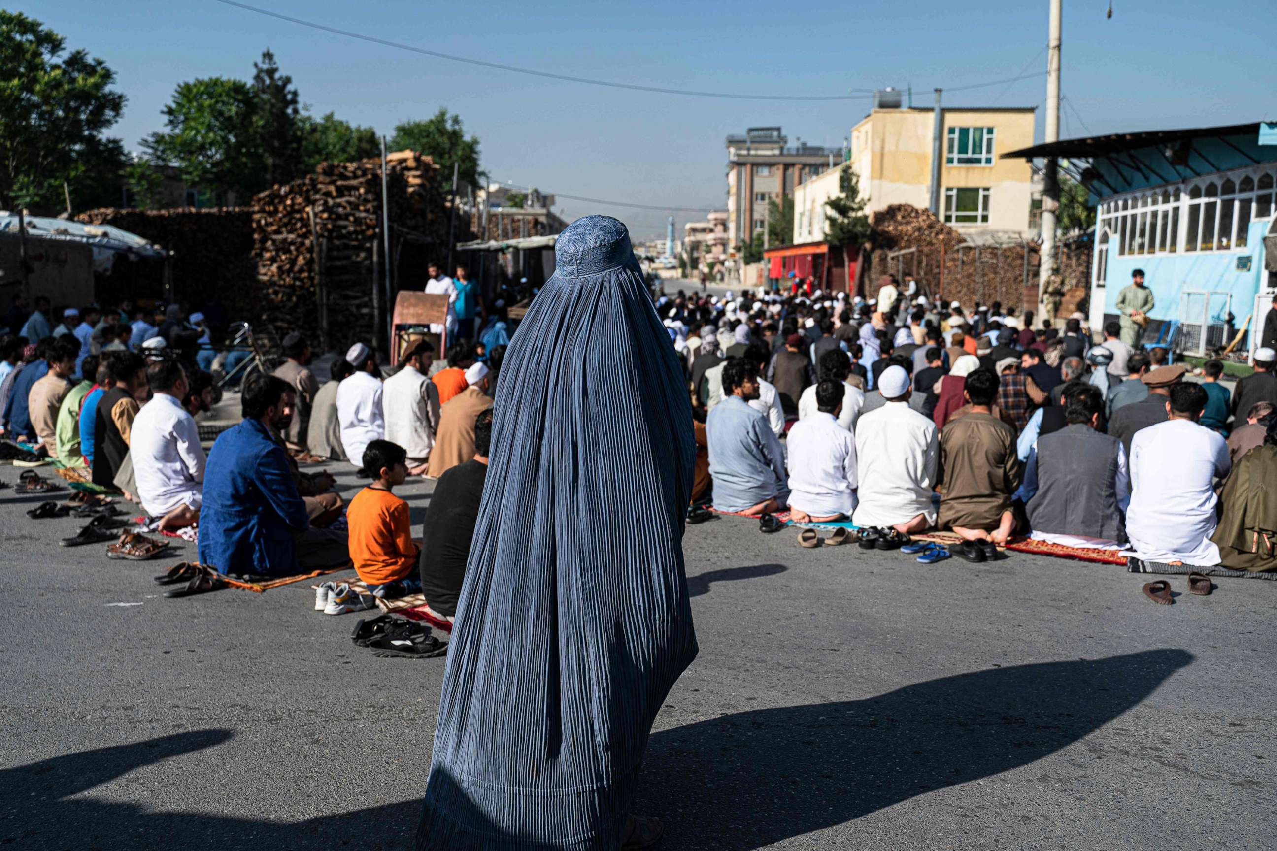 PHOTO: An Afghan burqa-clad woman stands as Muslim devotees offer Eid al-Fitr prayers, which marks the end of the holy fasting month of Ramadan outside a mosque in a street in Kabul, on May 1, 2022.