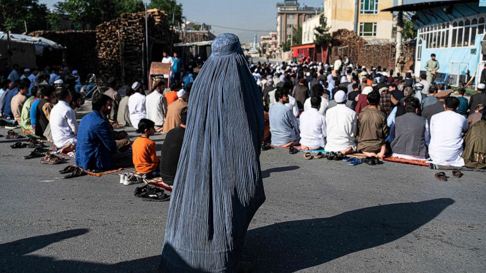 PHOTO: An Afghan burqa-clad woman stands as Muslim devotees offer Eid al-Fitr prayers, which marks the end of the holy fasting month of Ramadan outside a mosque in a street in Kabul, on May 1, 2022.
