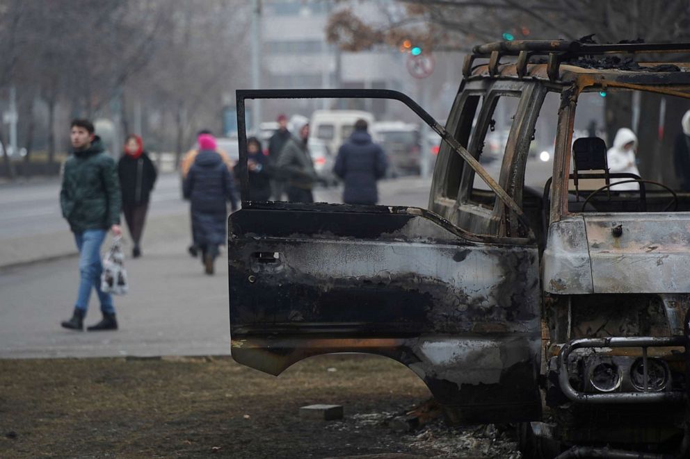 PHOTO: People walk past a bus, which was burned during clashes in Almaty, Kazakhstan, Jan. 11, 2022.