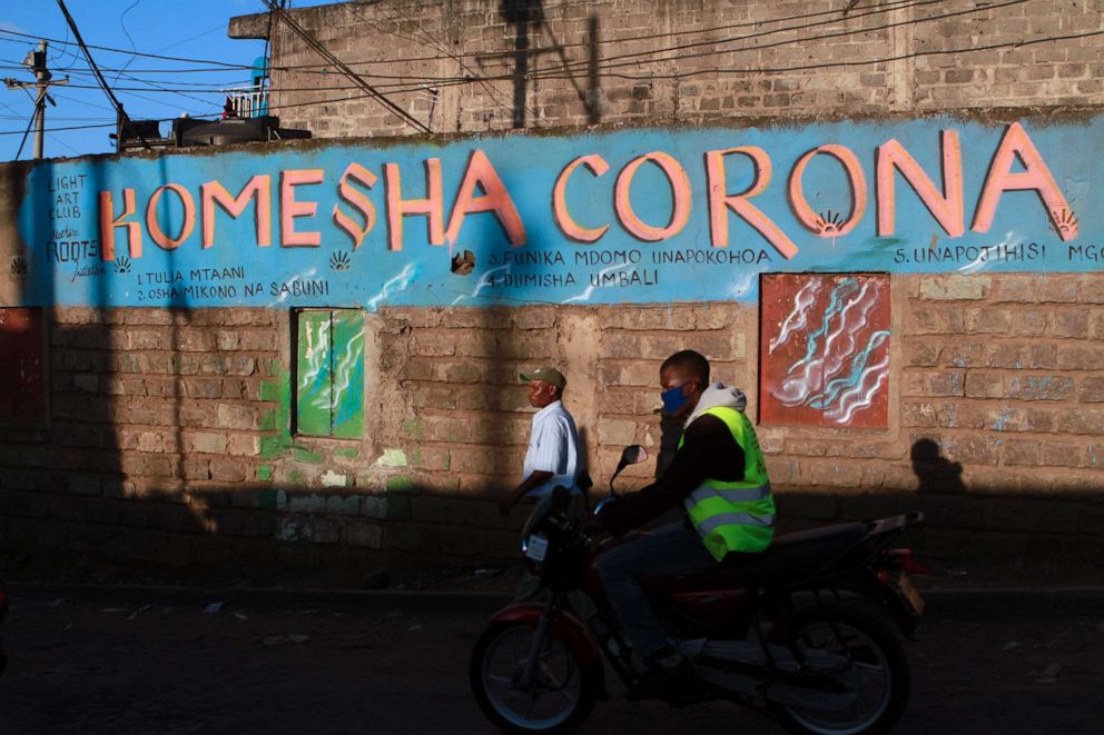 PHOTO: A motorcycle taxi rider cruises past a painted wall with the Swahili slogan that translates to "stop corona," in Nairobi, Kenya, April 8, 2020.