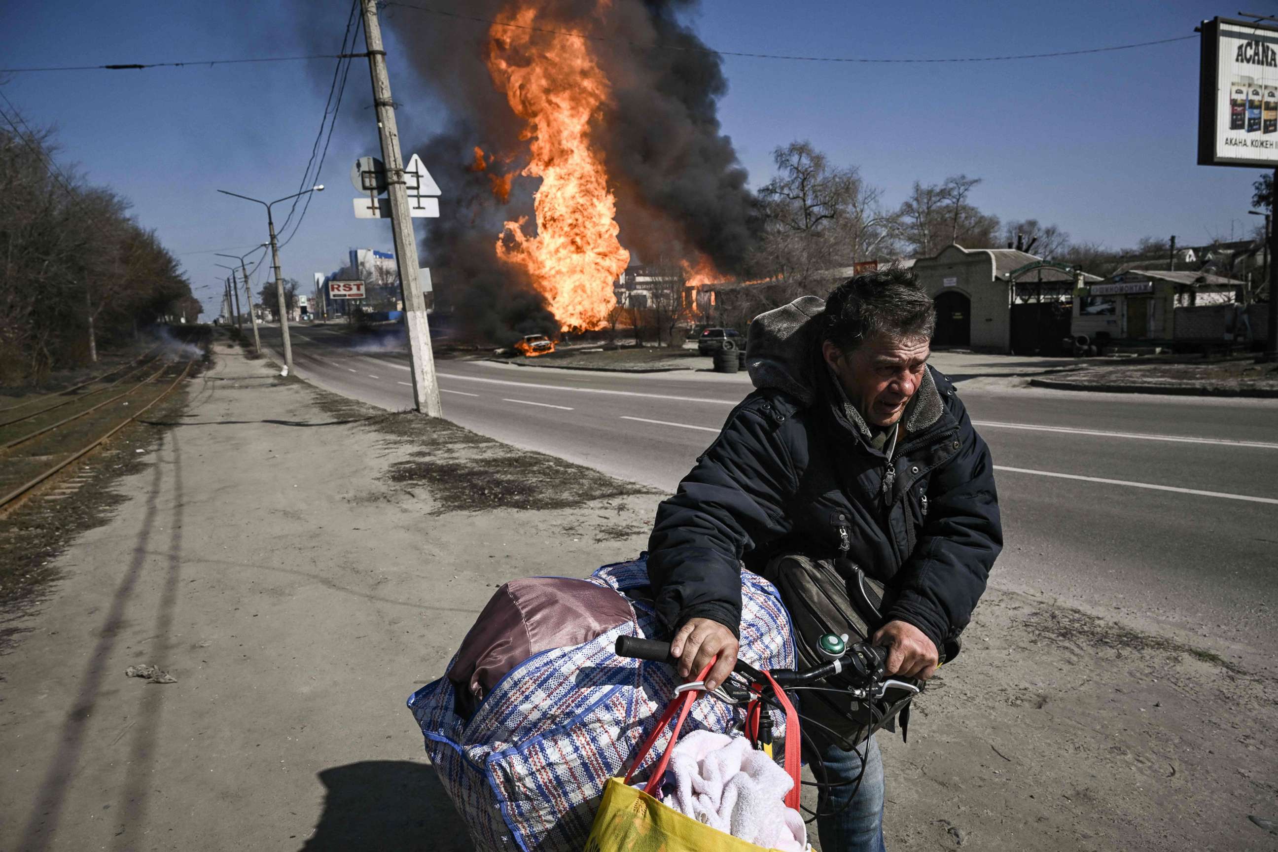 PHOTO: A man flees with his belongings as fire engulfs a vehicle and building followiA man flees with his belongings as fire engulfs a vehicle and building following artillery fire in the northeastern Ukrainian city of Kharkiv on March 25, 2022.