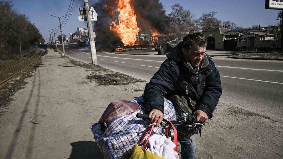 PHOTO: A man flees with his belongings as fire engulfs a vehicle and building followiA man flees with his belongings as fire engulfs a vehicle and building following artillery fire in the northeastern Ukrainian city of Kharkiv on March 25, 2022.