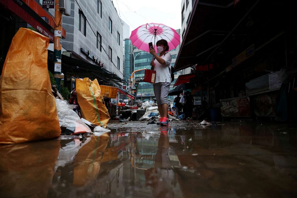 PHOTO: A woman using an umbrella takes photographs of a road that was flooded after torrential rain, at a traditional market in Seoul, South Korea, on Aug. 9, 2022.
