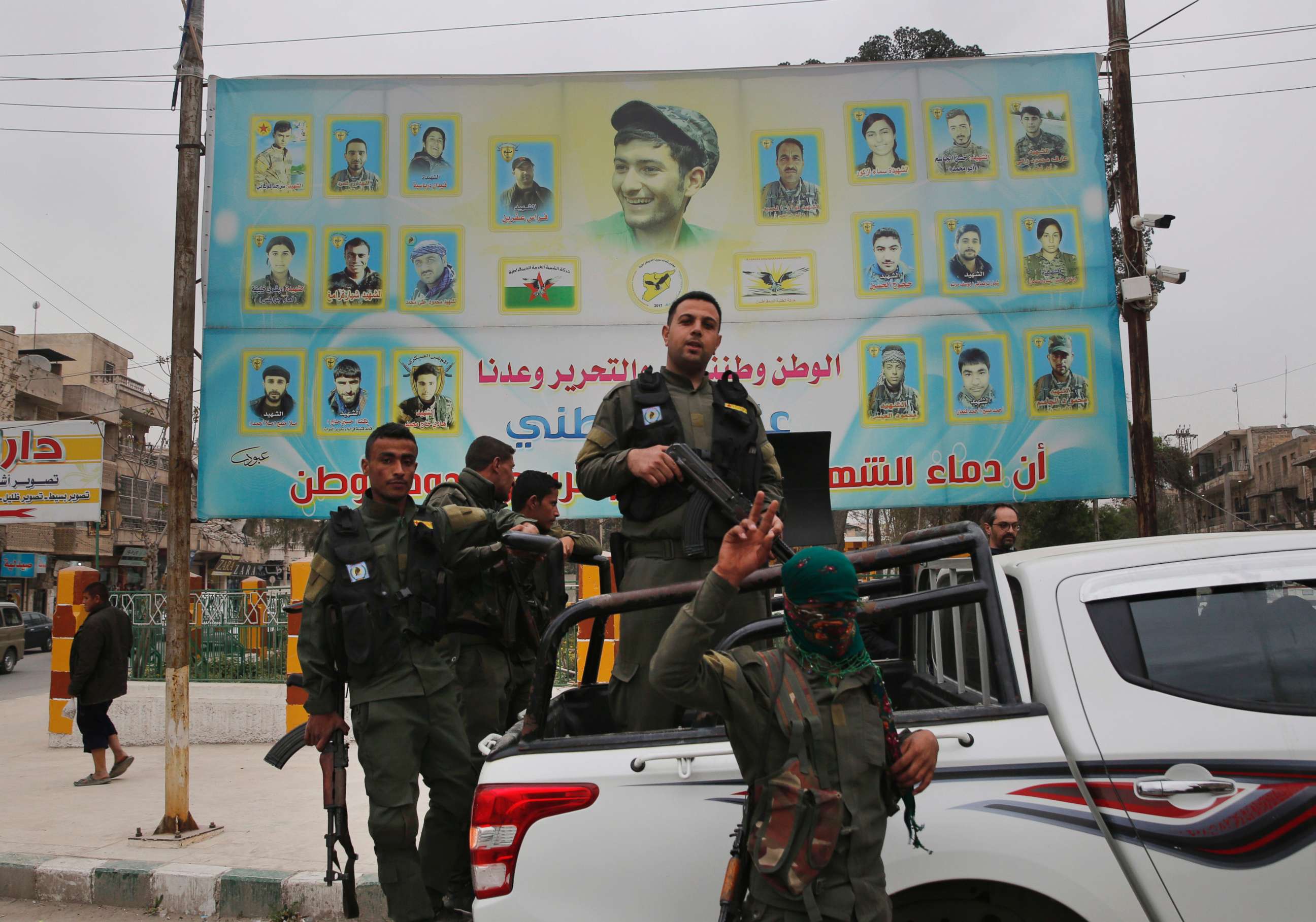 PHOTO: Members of the Kurdish internal security forces stand on their vehicle in front of a giant poster showing portraits of fighters killed fighting against the Islamic State group, in Manbij, Syria, March 28, 2018.