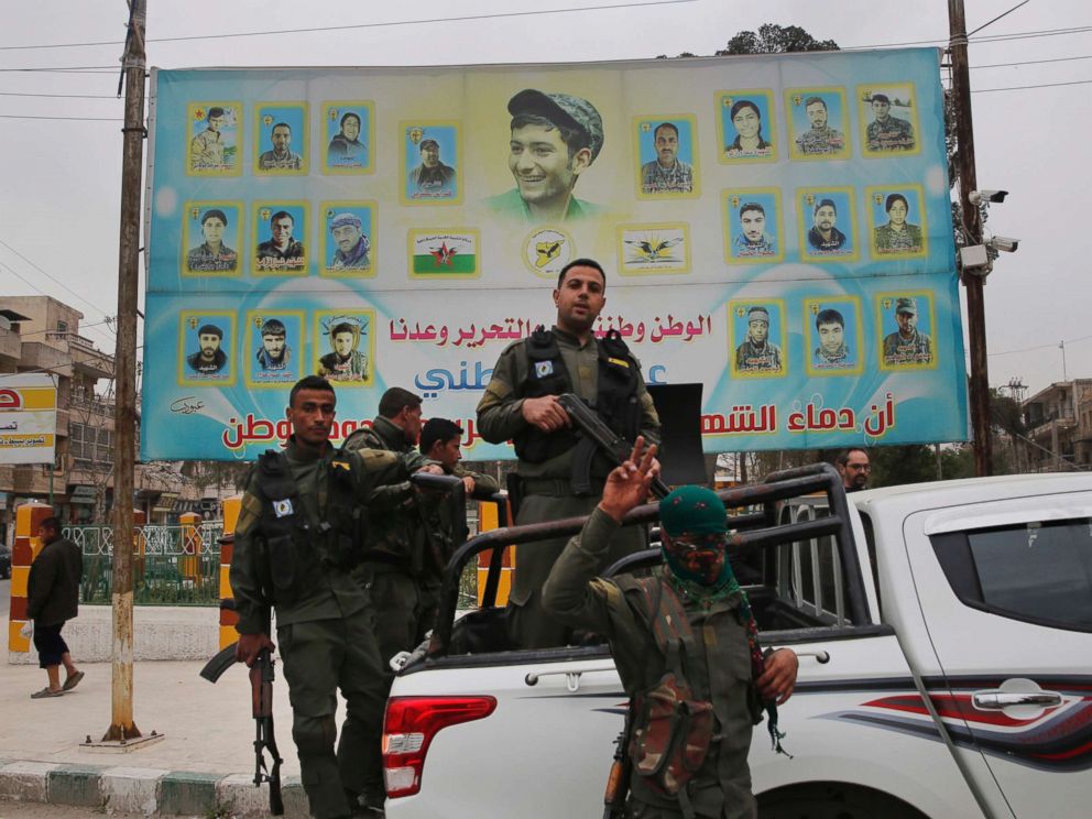 PHOTO: Members of the Kurdish internal security forces stand on their vehicle in front of a giant poster showing portraits of fighters killed fighting against the Islamic State group, in Manbij, Syria, March 28, 2018.