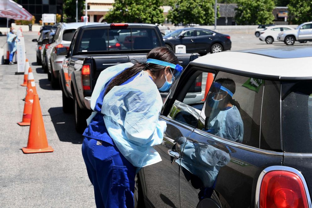 PHOTO: A worker wearing personal protective equipment (PPE) performs drive-up COVID-19 testing administered from a car, May 13, 2020, in the Sherman Oaks neighborhood of Los Angeles.