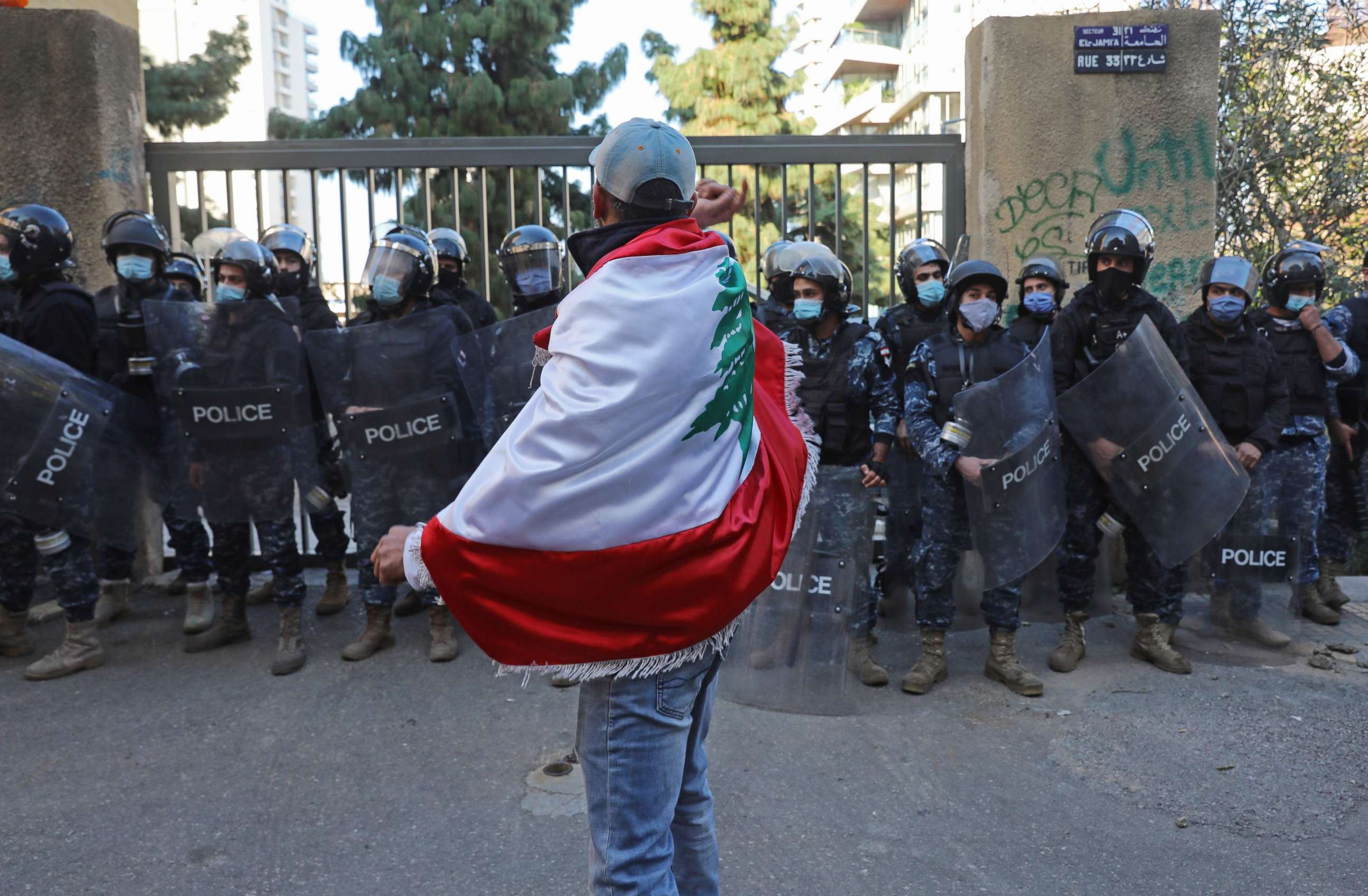 PHOTO: A protester draped in the national flag faces off with the police during a demonstration outside the entrance of the American University of Beirut, in the Lebanese capital's Bliss street on Dec. 29, 2020. 