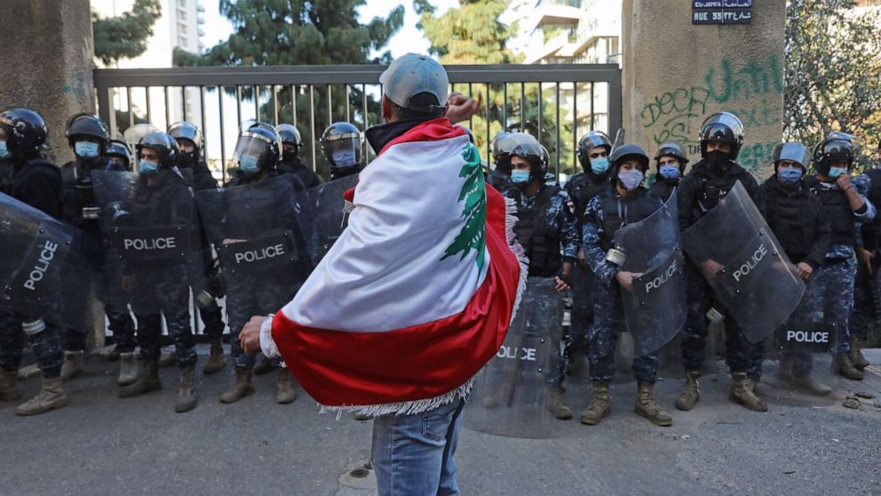PHOTO: A protester draped in the national flag faces off with the police during a demonstration outside the entrance of the American University of Beirut, in the Lebanese capital's Bliss street on Dec. 29, 2020. 