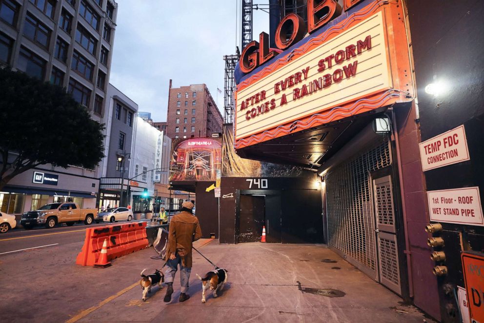 PHOTO: A pedestrian walks dogs past the shuttered Globe Theatre, with the message 'After Every Storm Comes a Rainbow' written on the marquee, during the coronavirus pandemic, March 23, 2019, in Los Angeles, Calif.