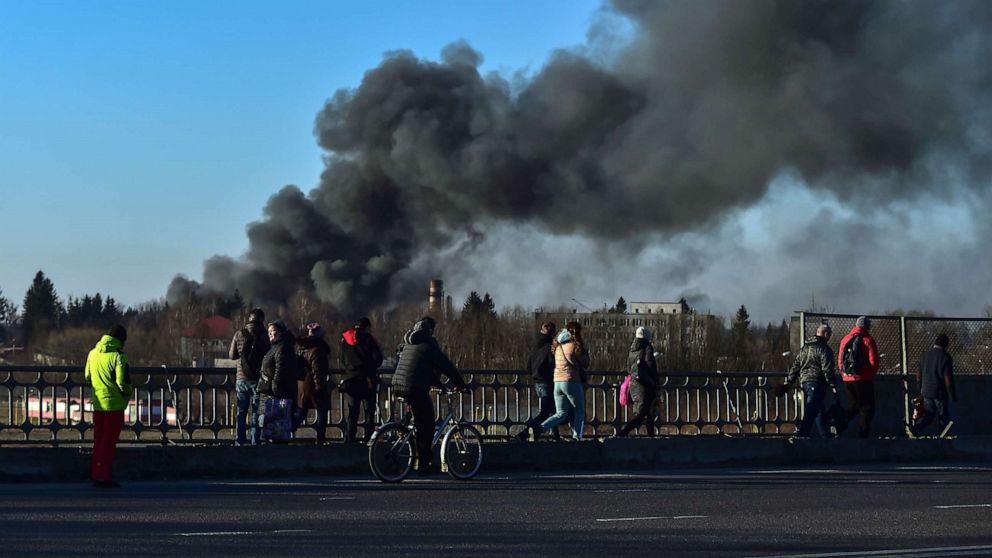 PHOTO: People walk as a cloud of smoke rises after an explosion near the airport, in Lviv, western Ukraine, March 18, 2022. The mayor of Lviv says missiles struck near the city's airport early Friday.