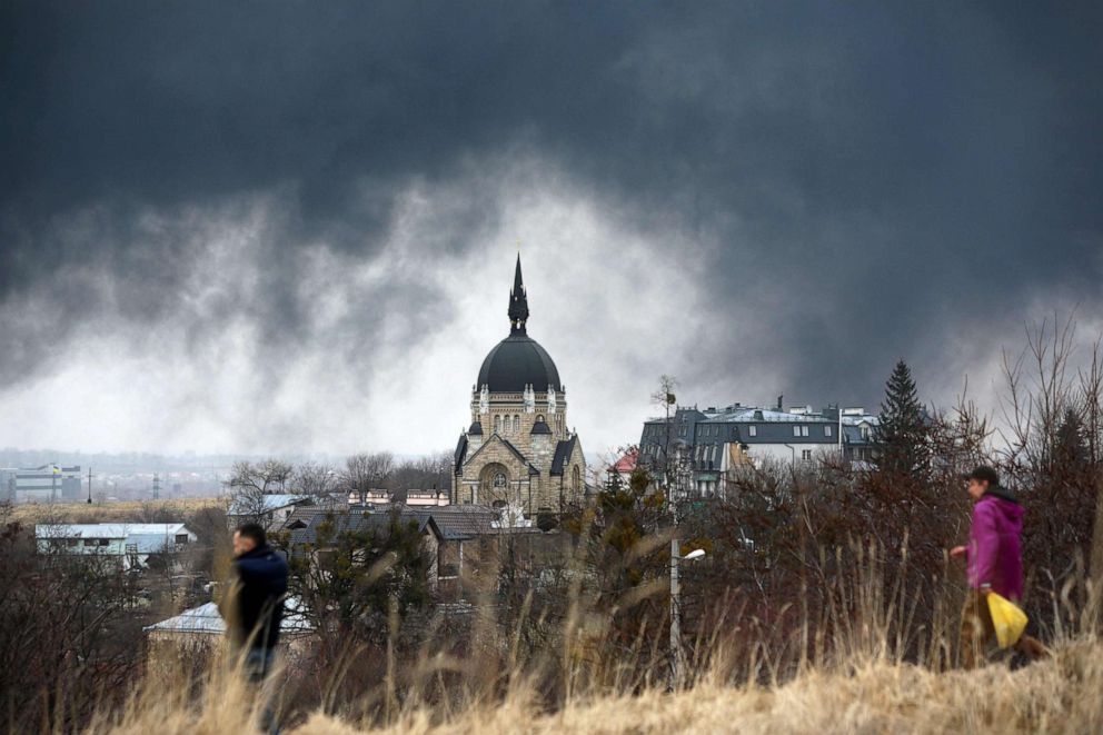 PHOTO: People walk in front of a church as smoke rises after an air strike in the western Ukrainian city of Lviv, on March 26, 2022.