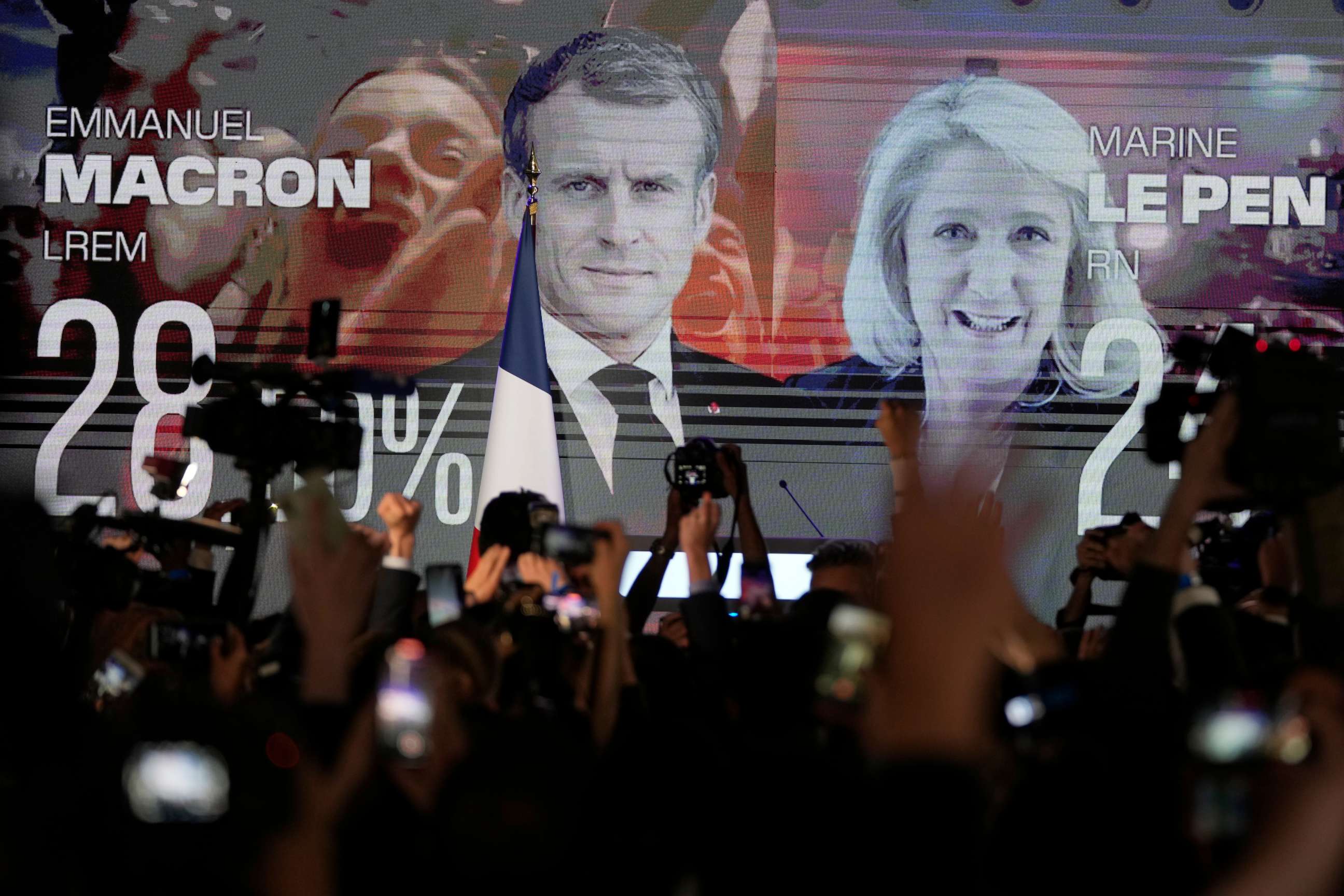 PHOTO: A screen shows French President Emmanuel Macron, centrist candidate for reelection, alongside far-right candidate Marine Le Pen at her election day headquarters, in Paris, April 10, 2022.