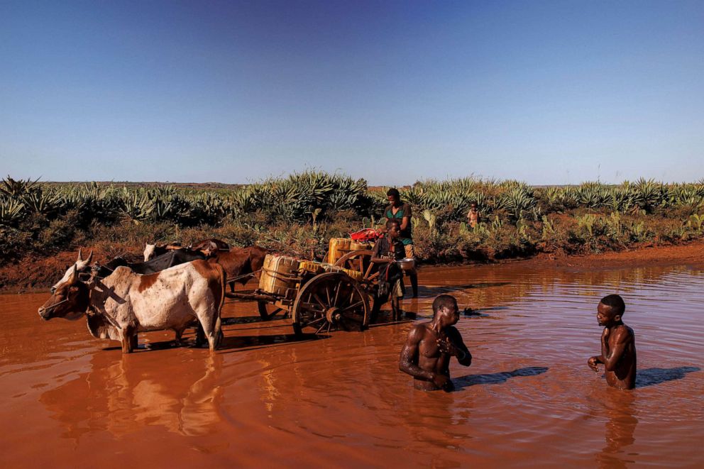 PHOTO: Two men bathe in rain water while two boys fill up plastic canisters with water, along the RN13 (National Road 13), near the town of Ambovombe, Madagascar, Feb. 14, 2022. 