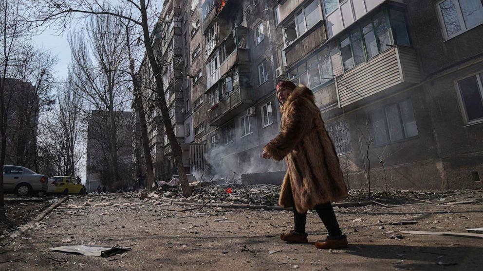 PHOTO: A woman walks past a burning apartment building after shelling in Mariupol, Ukraine, March 13, 2022.
