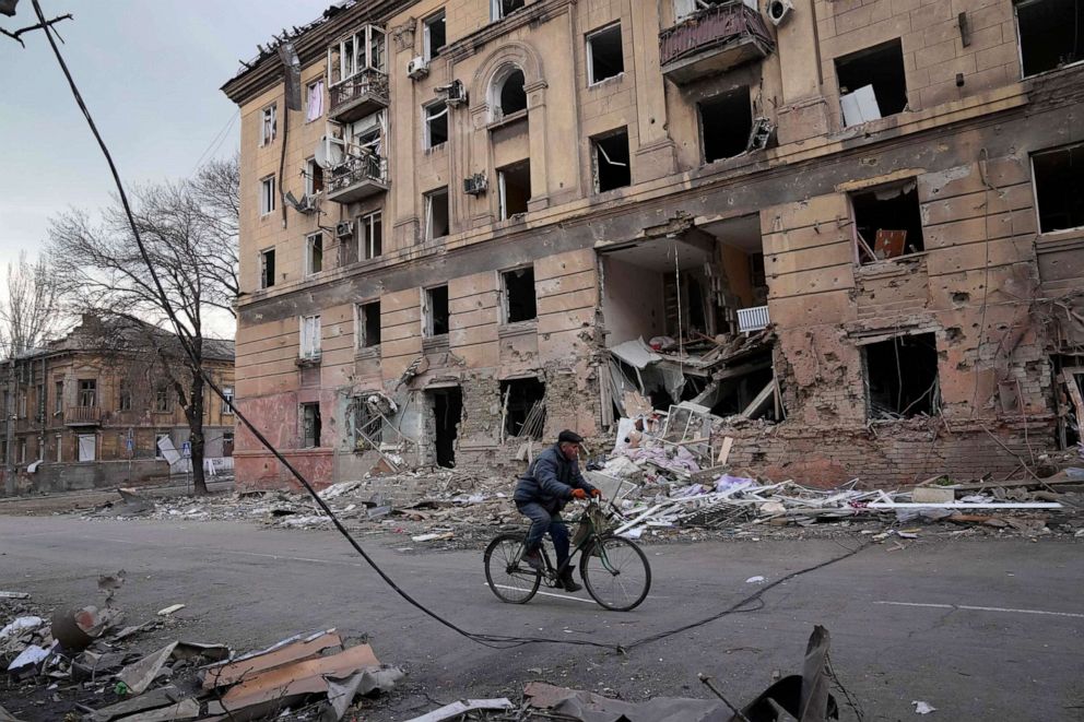 FOTOĞRAF: Bir adam, 9 Mart 2022'de Ukrayna'nın Mariupol kentinde bombardıman sonucu hasar gören bir apartmanın önünde bisiklete biniyor.