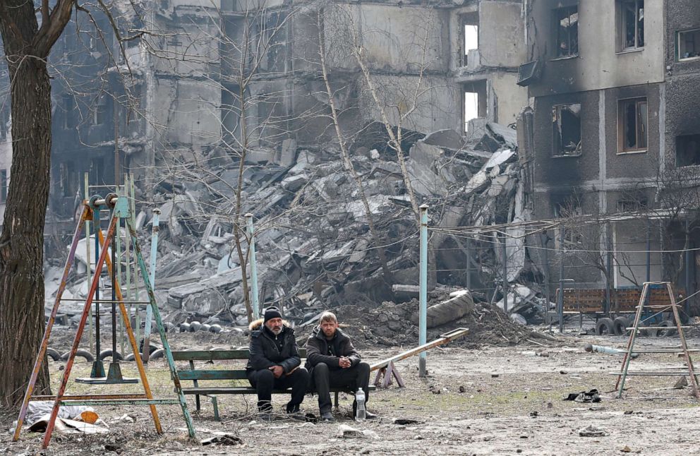 PHOTO: Local residents sit on a bench near a destroyed apartment building in the besieged southern port city of Mariupol, Ukraine on March 25, 2022.