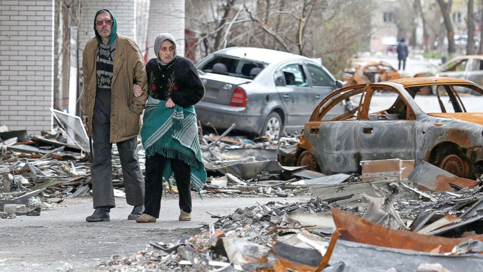 PHOTO: People walk past cars damaged during Ukraine-Russia conflict in the southern port city of Mariupol, Ukraine, April 21, 2022.