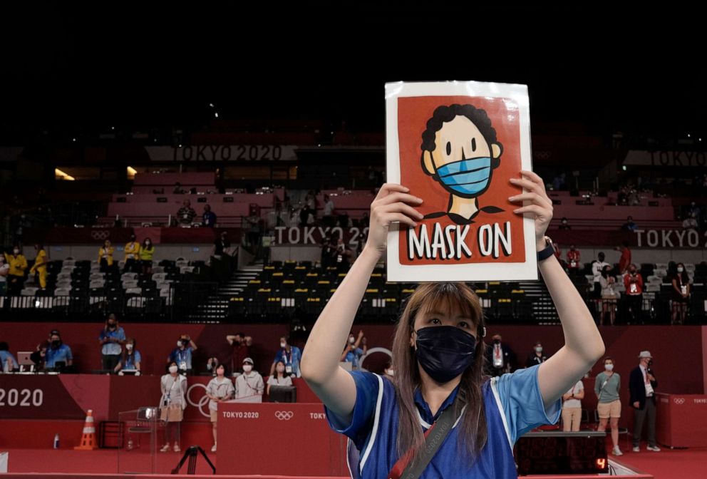 PHOTO: A volunteer holds a sign telling players to keep their masks on during the medals ceremony in women's volleyball at the 2020 Summer Olympics, Aug. 8, 2021, in Tokyo, Japan. 