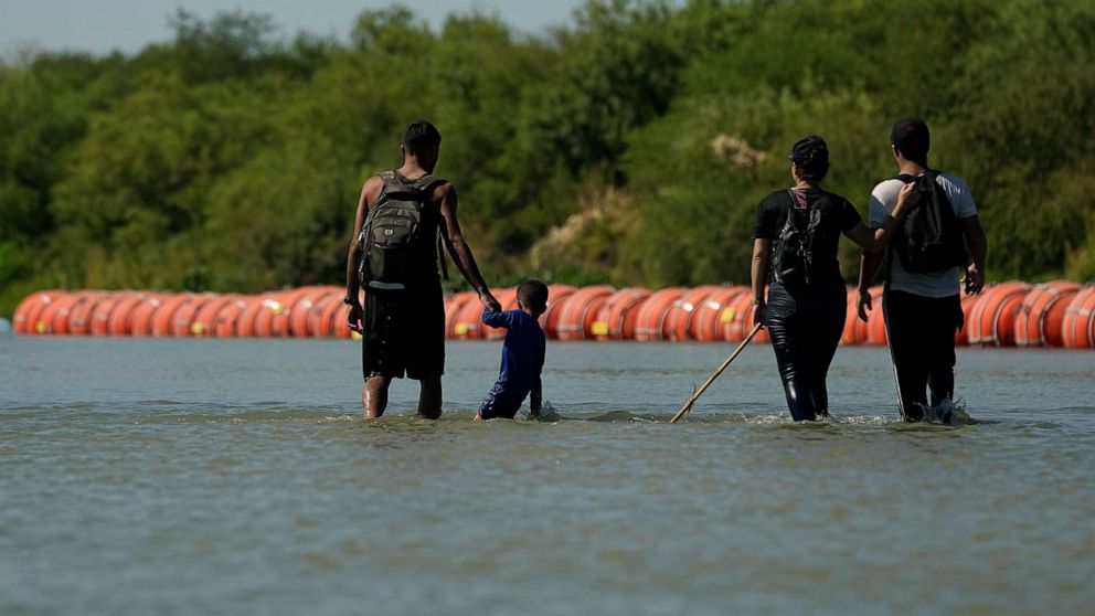 PHOTO: Migrants crossing into the U.S. from Mexico walk along large buoys being used as a floating border barrier on the Rio Grande Tuesday, Aug. 1, 2023, in Eagle Pass, Texas.