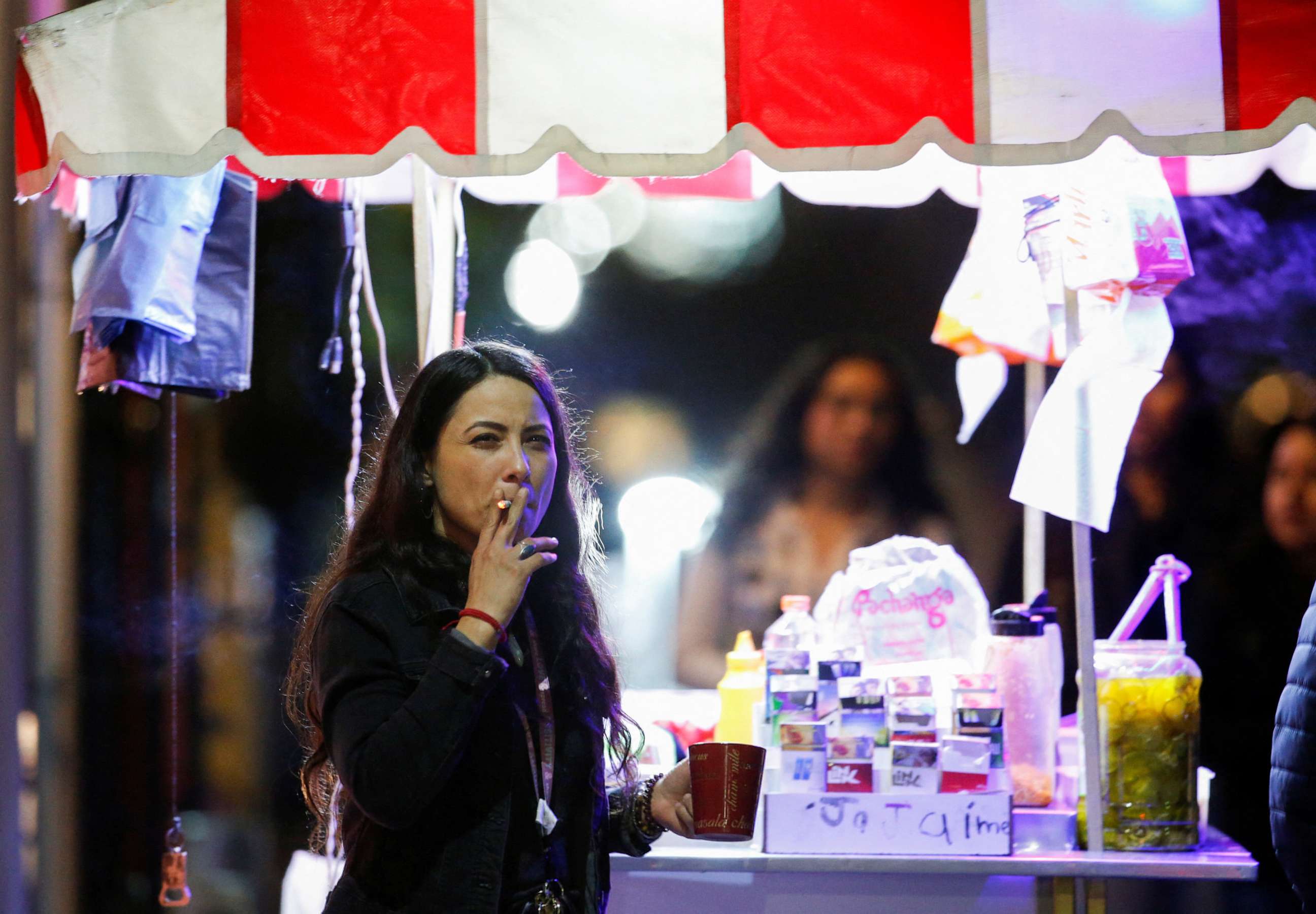 PHOTO: A woman smokes a cigarette next a food stall, before smoking was banned in public spaces according to a reform of the Mexican government's regulation of the general law for tobacco control, in Monterrey, Mexico, Jan. 14, 2023.