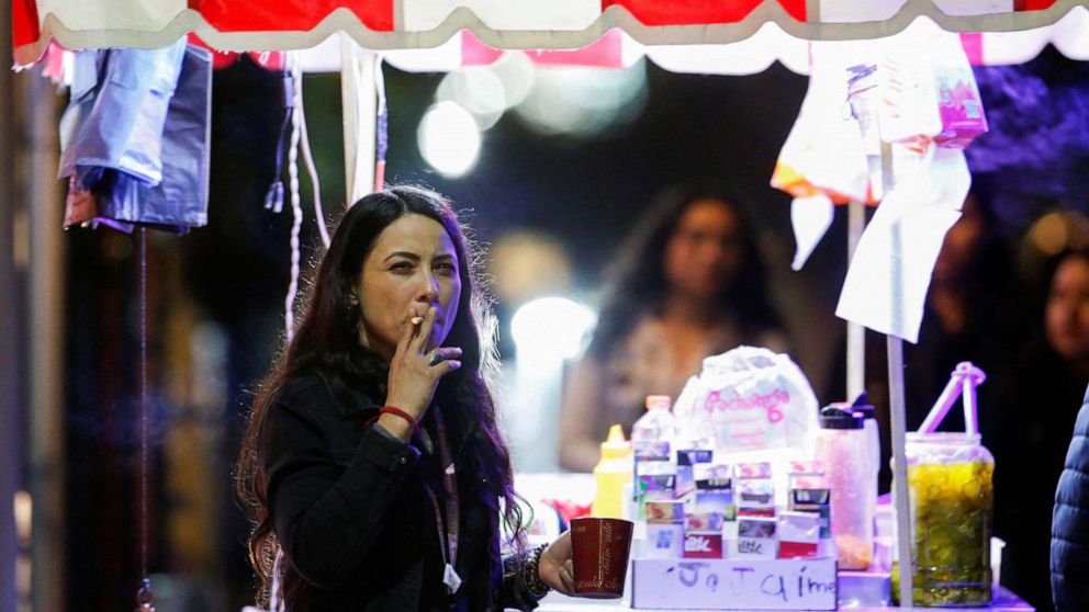 FOTO: Kobieta pali papierosa obok straganu z jedzeniem 14 stycznia 2023 r. w Monterrey w Meksyku, zanim reforma rządu meksykańskiego dotycząca ogólnej ustawy o kontroli tytoniu zakazała palenia w miejscach publicznych.