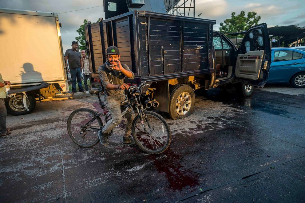 PHOTO: A man handles a bullet cartridge in a blooded street by a truck with a flat tire and covered with bullet hits after a gunfight in Culiacan, Mexico on Oct. 17, 2019.