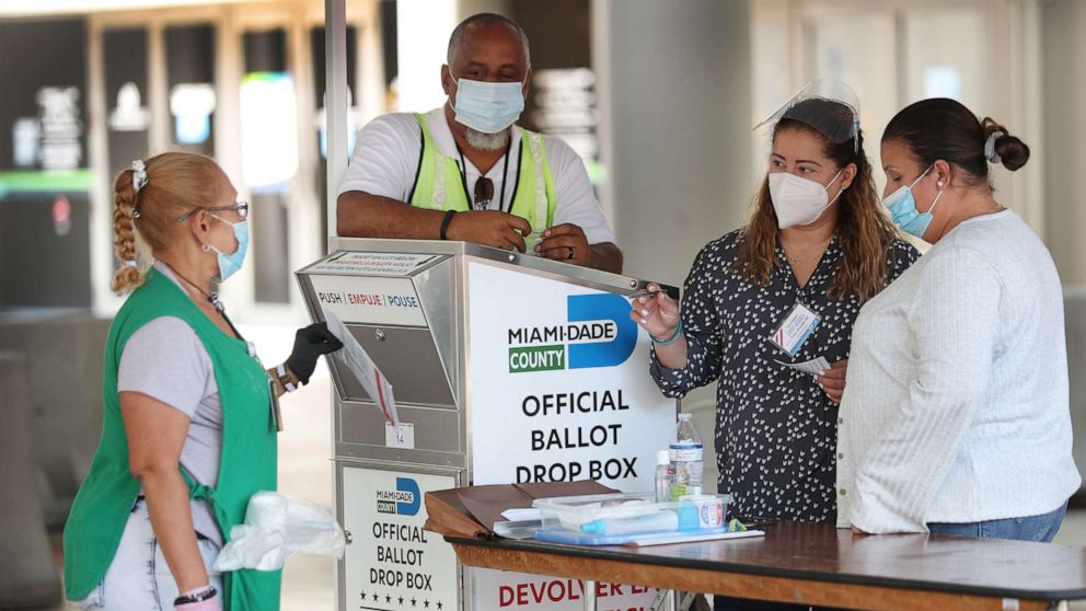 PHOTO: Poll workers help a voter put their mail-in ballot in an official Miami-Dade County ballot drop box on Aug. 11, 2020, in Miami.