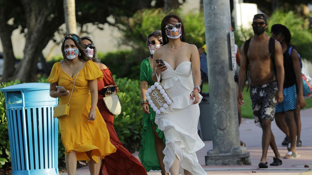 PHOTO: People wearing protective face masks walk along Ocean Drive during the coronavirus pandemic, July 24, 2020, in Miami Beach, Fla.