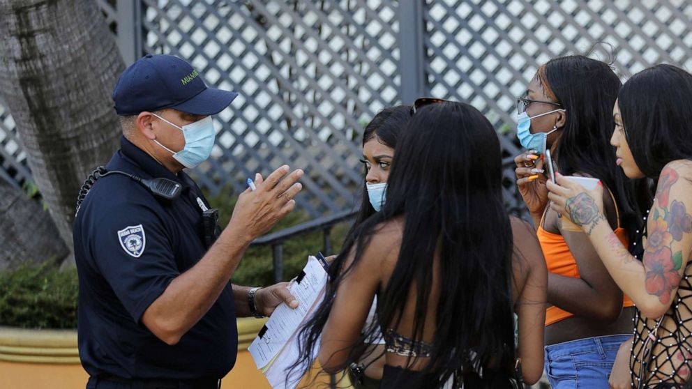 PHOTO: Luis Negron, a Miami Beach code compliance officer, left, talks with women along Ocean Drive about wearing a protective face mask amid the coronavirus pandemic, July 24, 2020, in Miami Beach, Fla.
