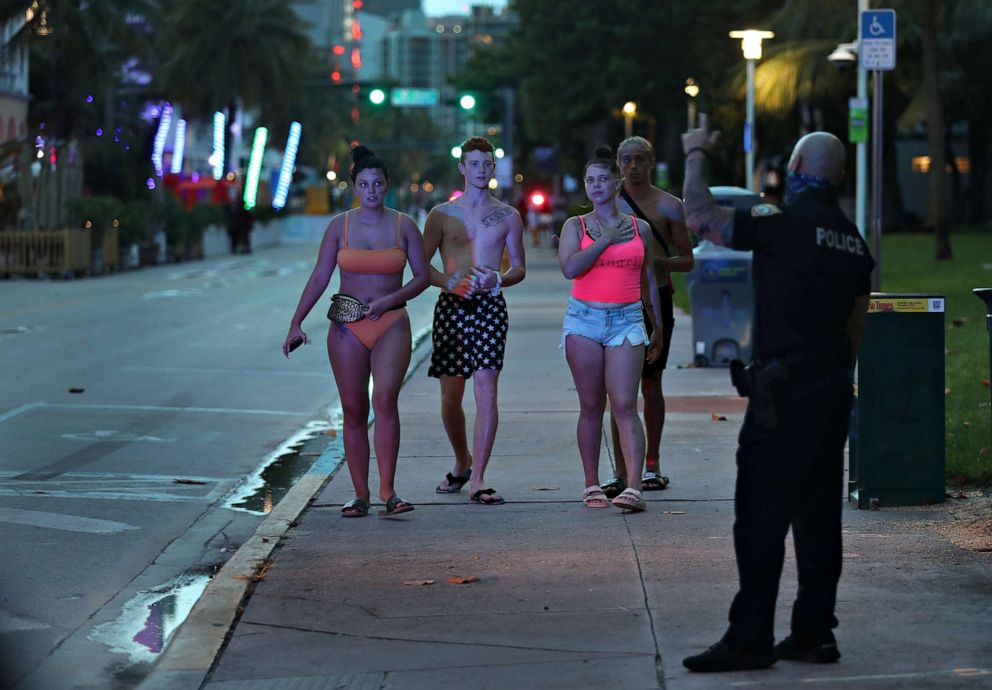 PHOTO: A Miami Beach police officer directs people out of the entertainment district as a curfew from 8pm to 6am is put in place to combat the spread of the coronavirus on July 18, 2020, in Miami Beach, Fla.
