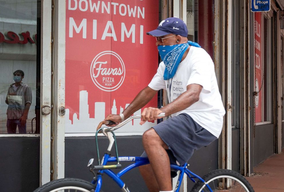 PHOTO: A man rides a bike covering his face in Downtown Miami, July 22, 2020.