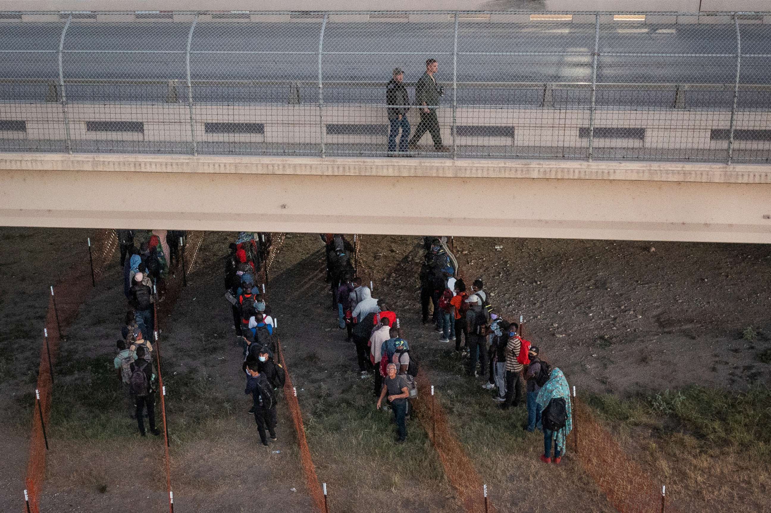 PHOTO: Law enforcement officials walk overhead as migrants await to get on a Customs and Border Protection bus out of a makeshift camp along the International Bridge in Del Rio, Texas, Sept. 24, 2021.