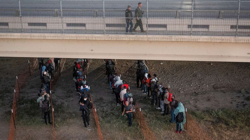 PHOTO: Law enforcement officials walk overhead as migrants await to get on a Customs and Border Protection bus out of a makeshift camp along the International Bridge in Del Rio, Texas, Sept. 24, 2021.