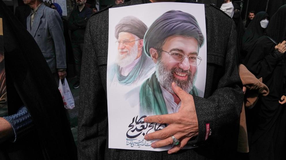 PHOTO: A mourner holds a poster depicting Ayatollah Mojtaba Khamenei, right, the successor to his late father Ayatollah Ali Khamenei, left, as supreme leader, in Tehran, Iran, Wednesday, March 11, 2026.