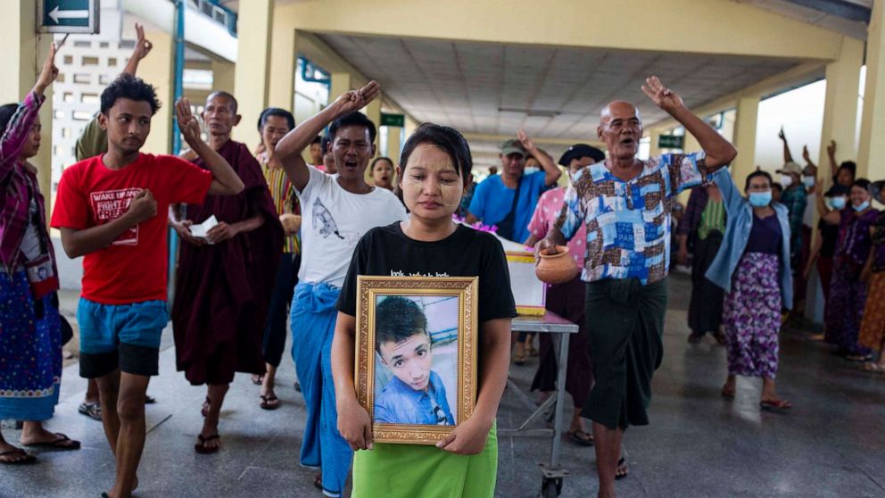 PHOTO: A relative holds the portrait of a man killed on March 14th by security forces while protesters make the three finger salute in Yangon, Myanmar, March 16, 2021.