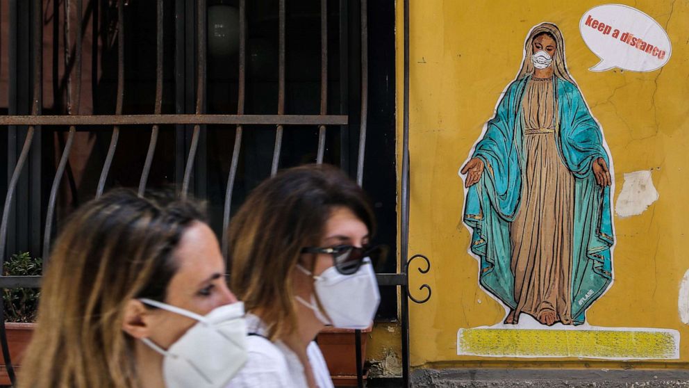 PHOTO: Women wearing a face masks walk past a mural by Art Flase depicting the Virgin Mary wearing a mask and saying "Keep a distance" in downtown Naples, Italy, on May 13, 2020.