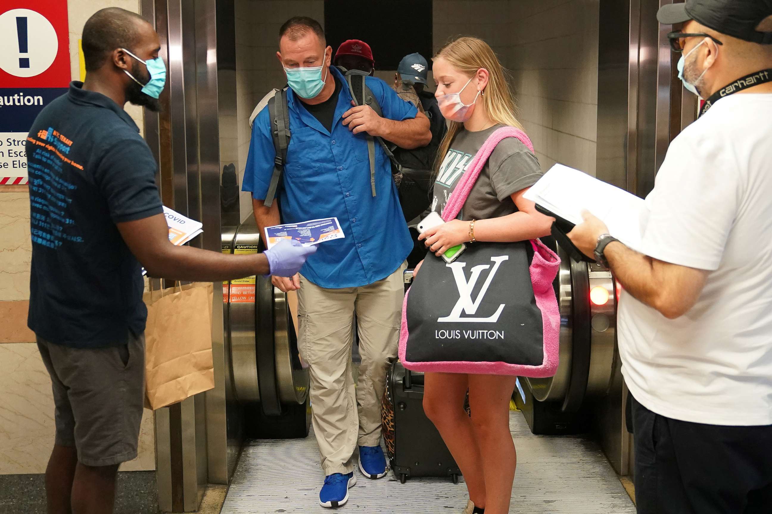 PHOTO: Passengers on a train from Florida stop and register with officials at Penn Station during an effort to screen out-of-state travelers and enforce the state's 14-day COVID-19 quarantine in New York, Aug. 6, 2020. 