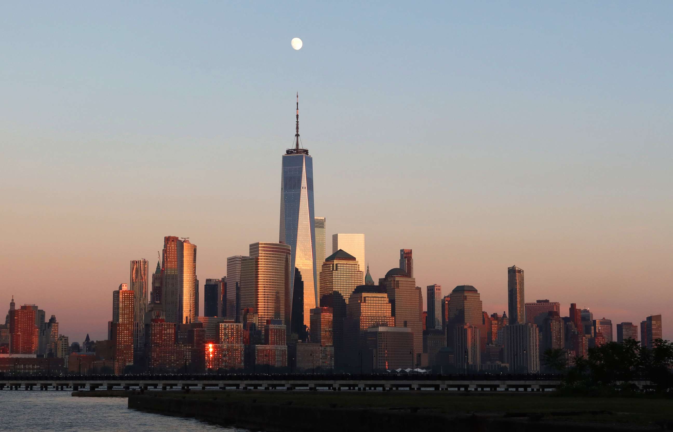 PHOTO: The moon rises as the sun sets on the skyline of lower Manhattan and One World Trade Center in New York City on July 31, 2020, as seen from Jersey City, New Jersey.