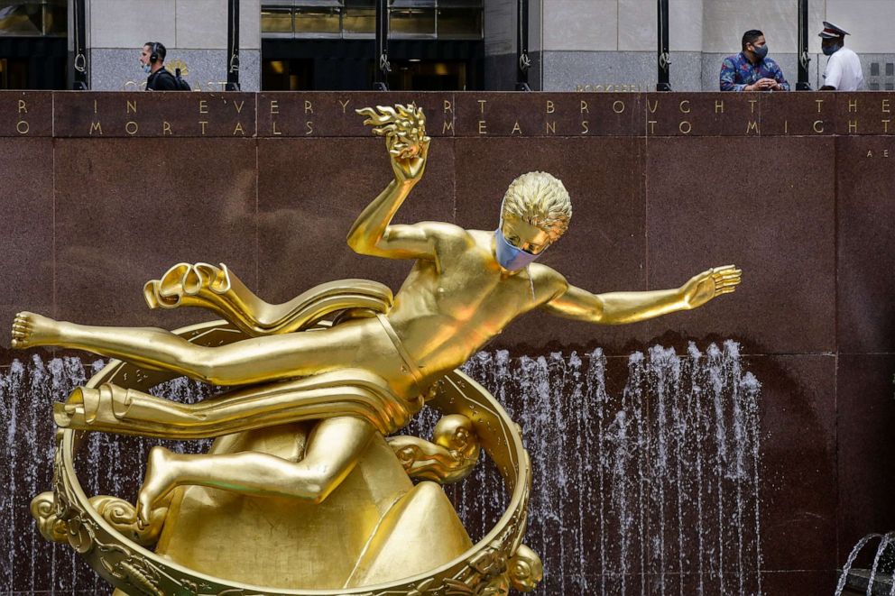 PHOTO: Pedestrians wearing masks walk past a statue of Prometheus, also wearing a mask, at Rockefeller Center in midtown Manhattan in New York, July 8, 2020.