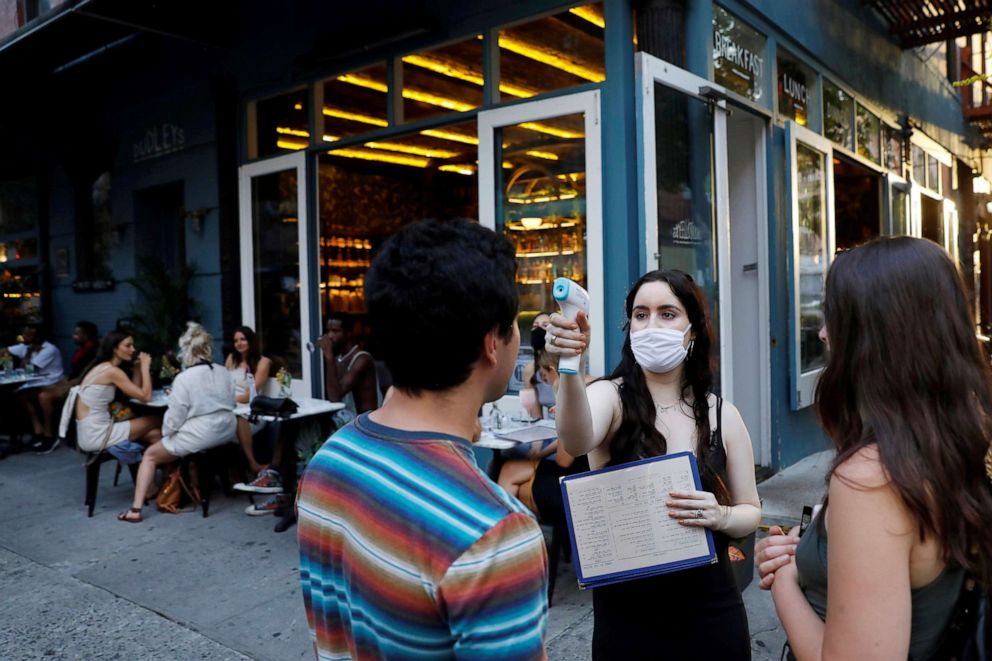 PHOTO: A waitress takes the temperature of customers at Dudley's as restaurants are permitted to offer al fresco dining as part of phase 2 reopening during the coronavirus pandemic in the Lower East Side of Manhattan in New York City, June 27, 2020.