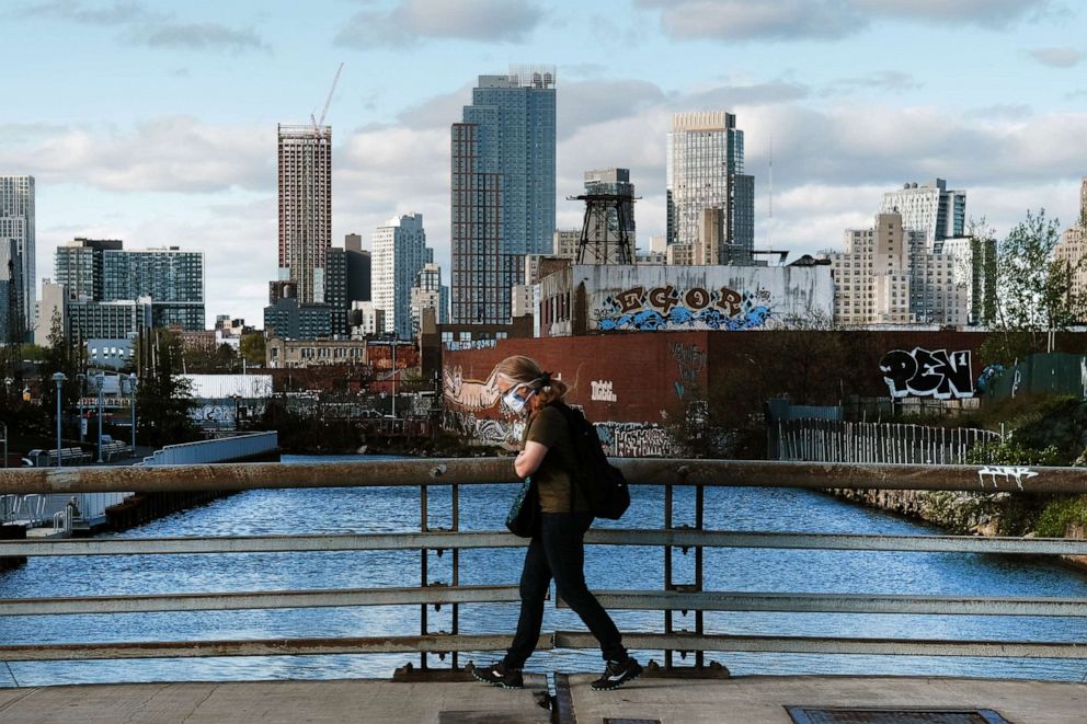 PHOTO: A pedestrian in protective mask walks past a view of downtown Brooklyn, May 4, 2020, in New York City.