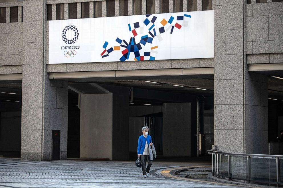 PHOTO: A woman walks beneath a Tokyo 2020 Olympics banner, March 19, 2020, in Tokyo, Japan. 