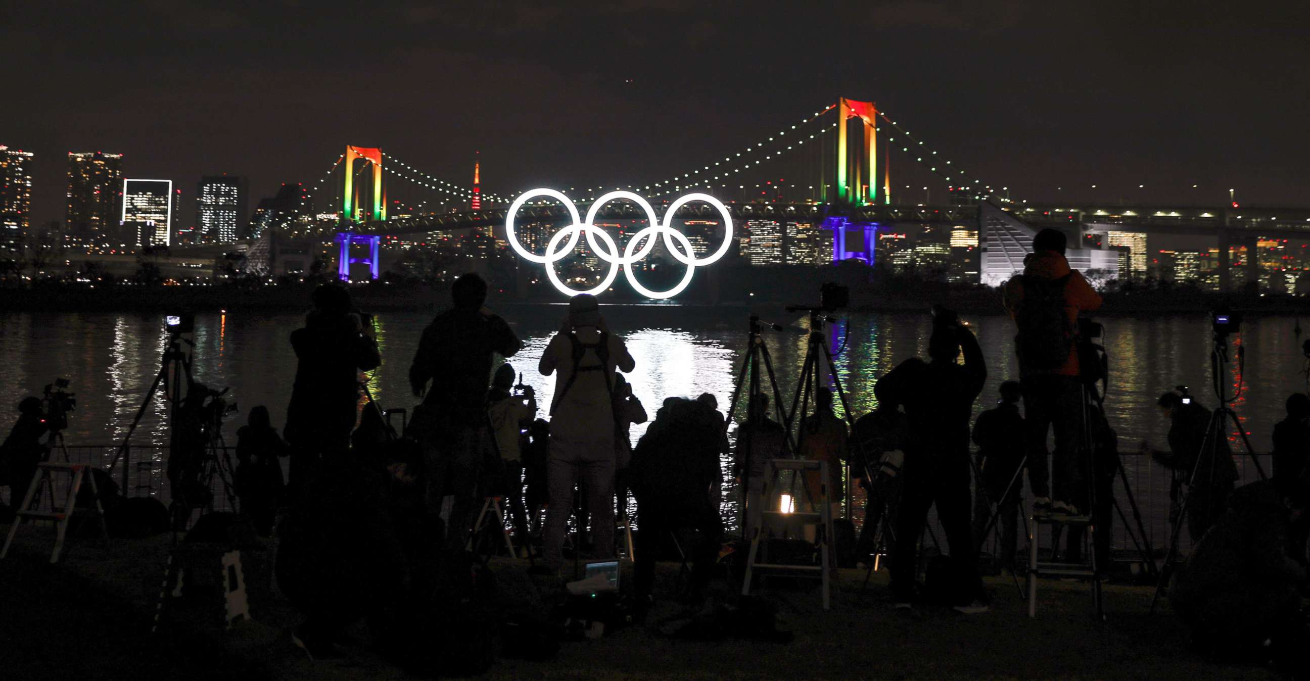 PHOTO: Journalists take images of the illuminated Olympic Rings monument at Odaiba Marine Park as the Rainbow Bridge is illuminated in rainbow colors to mark half a year before the opening of the Tokyo 2020 Olympic Games in Tokyo, Japan, Jan. 24, 2020. 