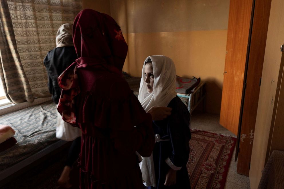 PHOTO: A girl at the orphanage helps Samira, 9, put on her chaddor before going to school, in her room at the orphanage in Kabul, Afghanistan, Oct. 12, 2021. 