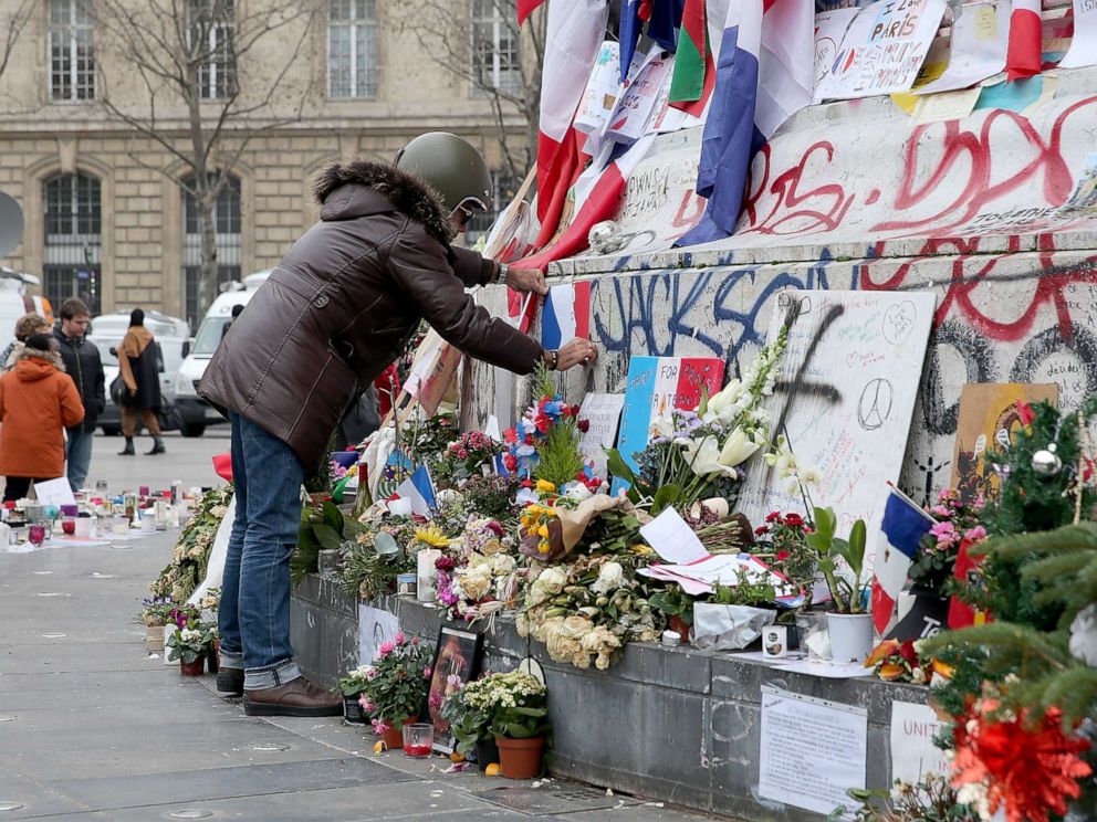 PHOTO: A man is seen posting a French flag on the monument of the Place de la Republique where people continue to pay tribute to the Paris Attacks victims one month after they occurred, Dec. 13, 2015, in Paris.