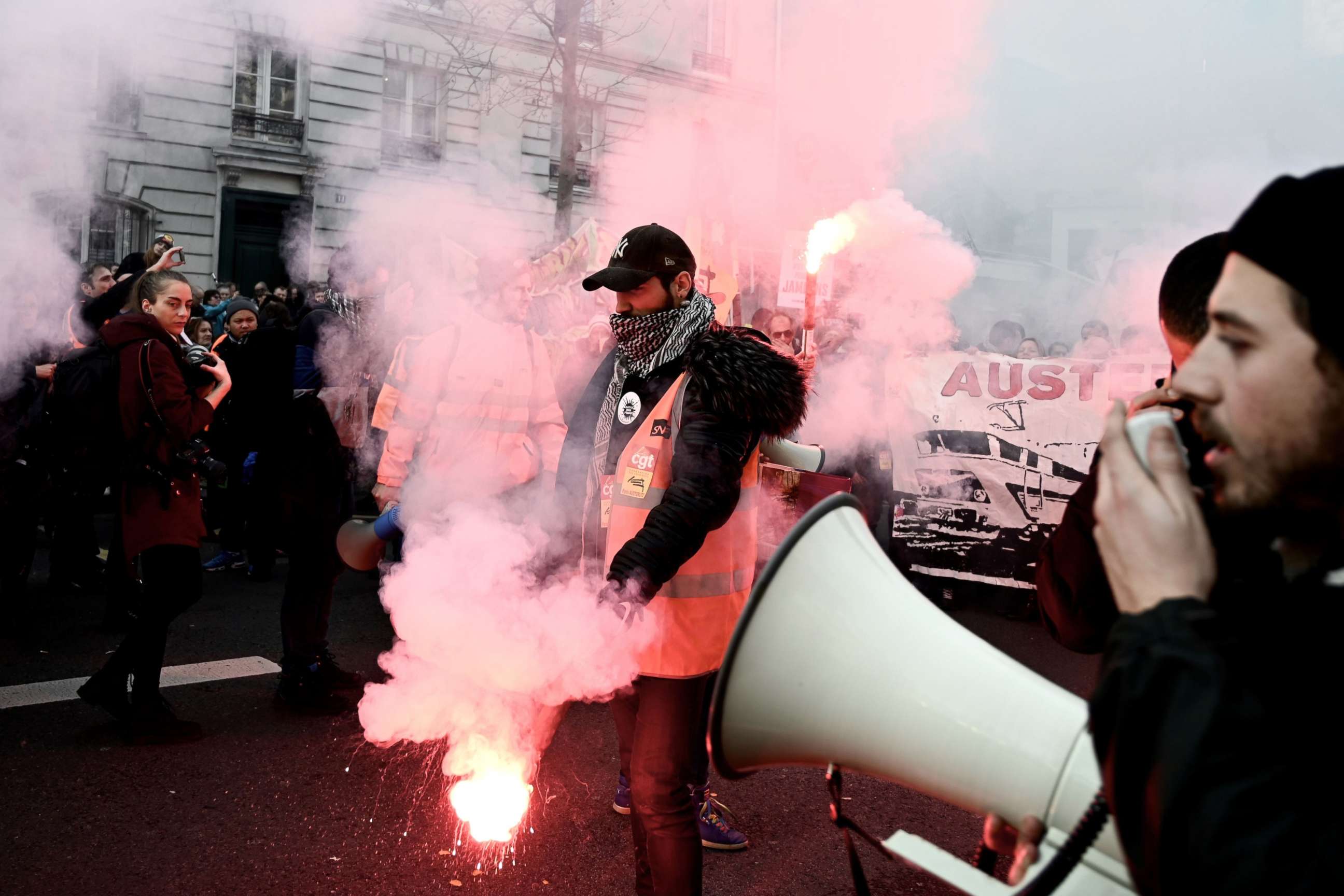 PHOTO: A man with a vest of the French state railway company SNCF burns flares next to a man speaking in a loud speaker during a demonstration in Paris, Dec. 17, 2019.