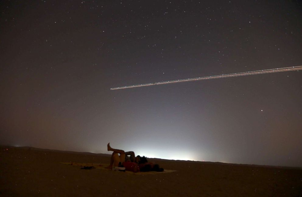 PHOTO: People lie on the ground to watch the Perseid meteor shower as an airplane flies over the Al Qudra desert, in Dubai, United Arab Emirates, Aug. 12, 2018.