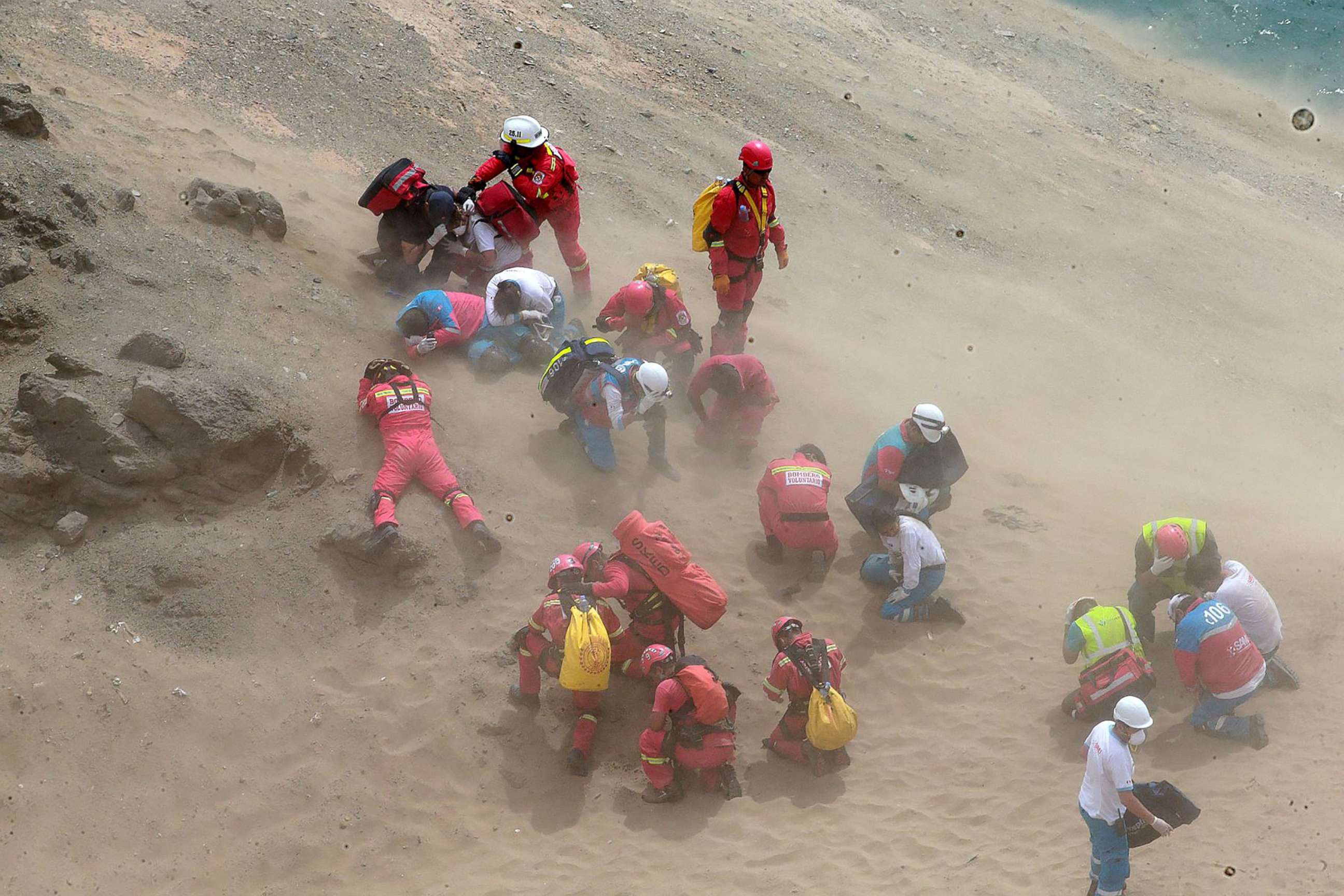 PHOTO: Emergency personnel covering themselves from dust generated by a helicopter during rescue operations after a passenger bus plunged off the Pan-American Highway North, outside of Lima, Peru, Jan. 2, 2018. 