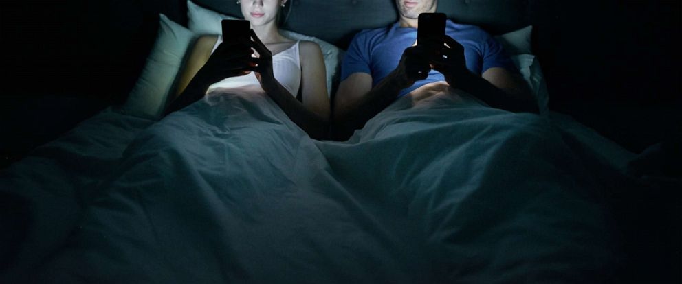 PHOTO: A young couple on iphones in bed. 