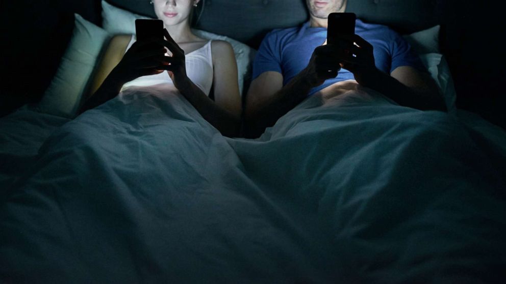 PHOTO: A young couple on iphones in bed.